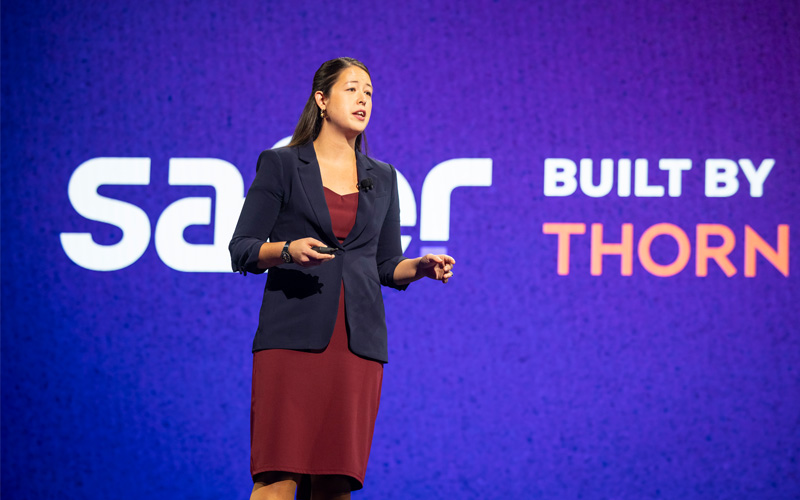 Rebecca Portnoff, wearing a red dress and dark blue blazer, speaking on stage as a keynote speaker
